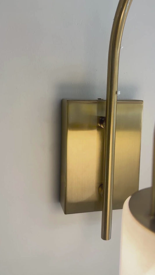 Modern brass and alabaster marble wall sconce with curved arm and soft lighting.