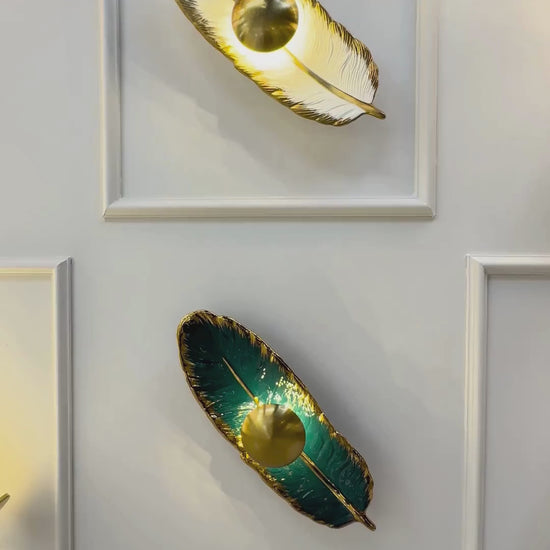 Horizontally placed feather wall light in emerald porcelain and brass finish with LED lighting, enhancing a contemporary interior wall.