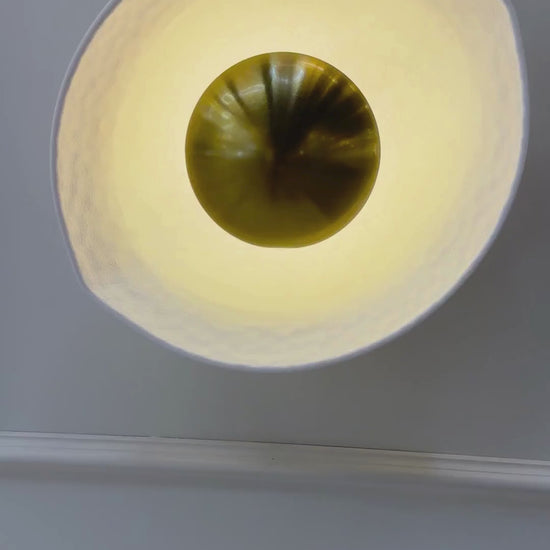 Side view of a deco wall sconce with golden core and softly illuminated hammered white shade.