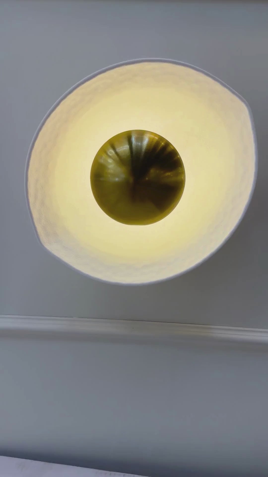 Side view of a deco wall sconce with golden core and softly illuminated hammered white shade.