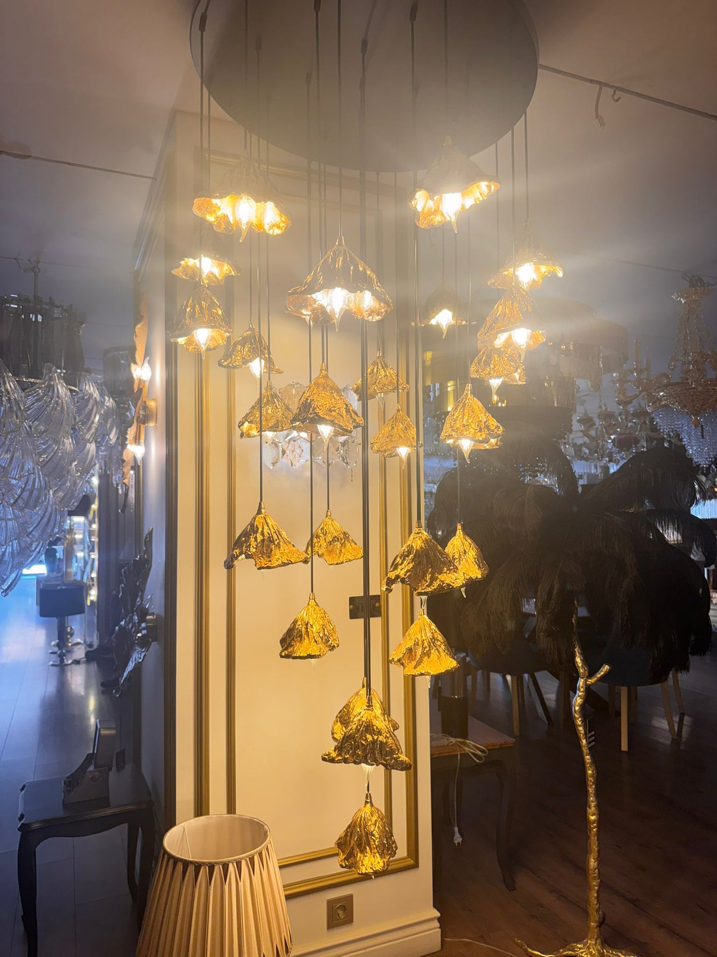 Bright pure brass leaf pendant lights forming a radiant chandelier in a luxury showroom.