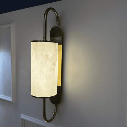 Angled close-up of illuminated brass wall sconce with alabaster shade and side lighting glow.