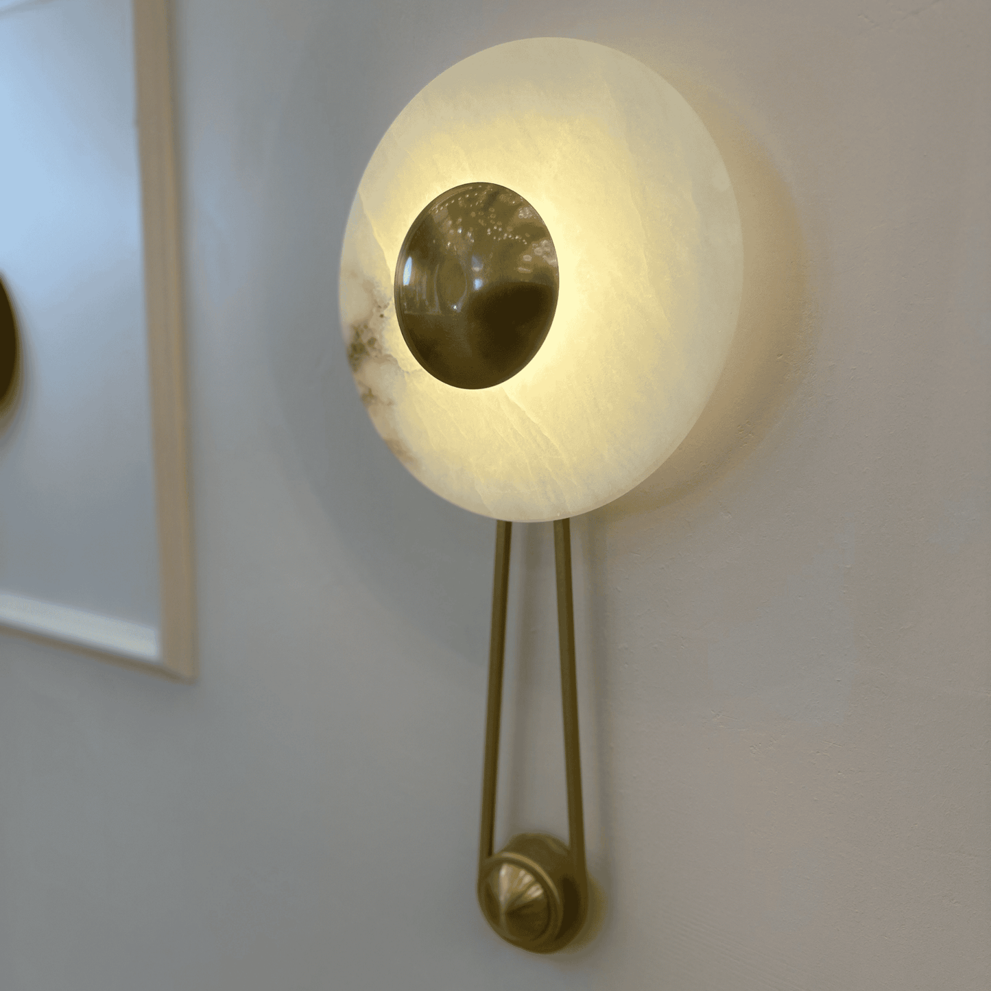 Side view of round alabaster sconce with central brass disc on an interior wall.