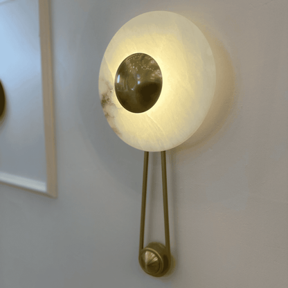 Side view of round alabaster sconce with central brass disc on an interior wall.