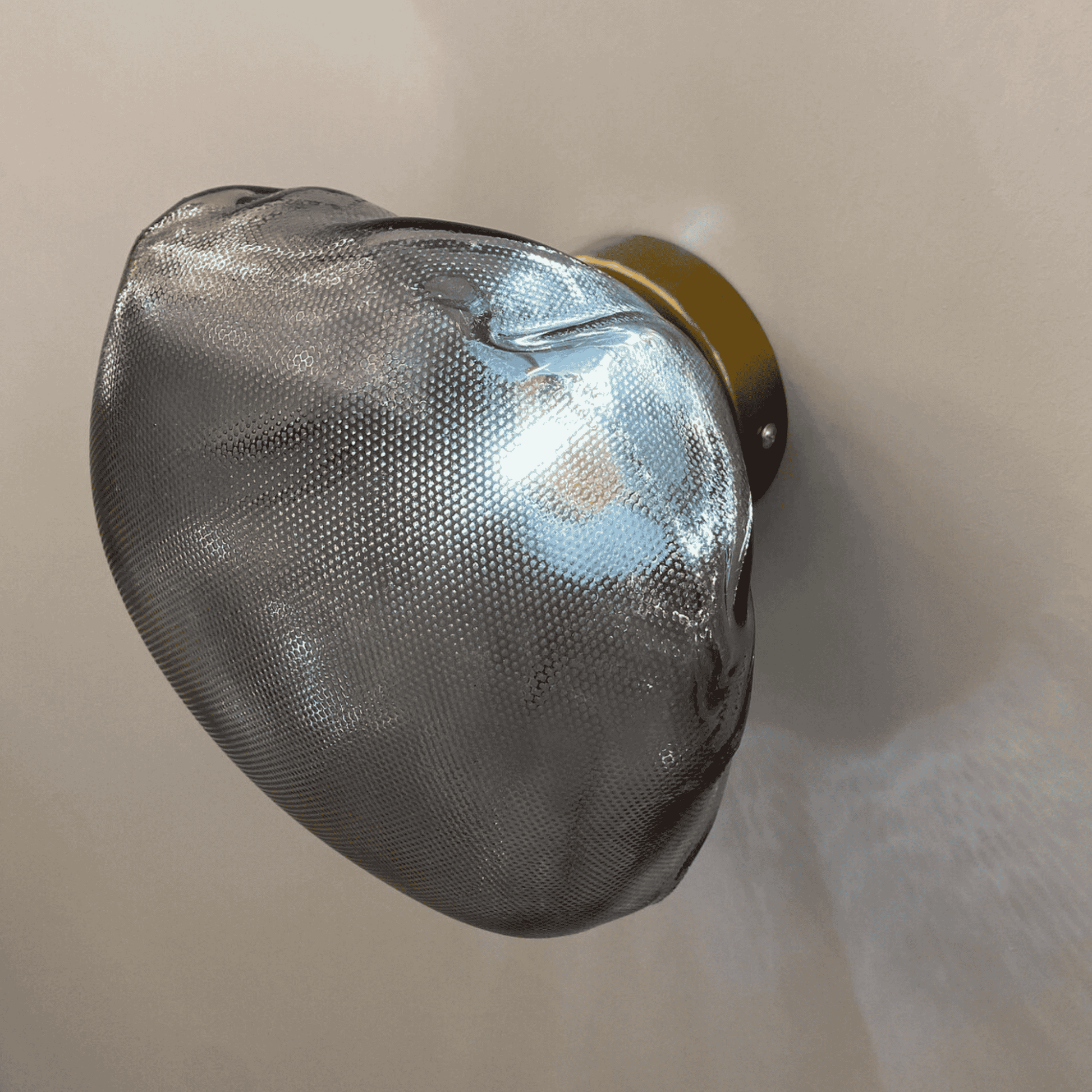Side angle of smoky stone-shaped glass wall sconce mounted on neutral wall.