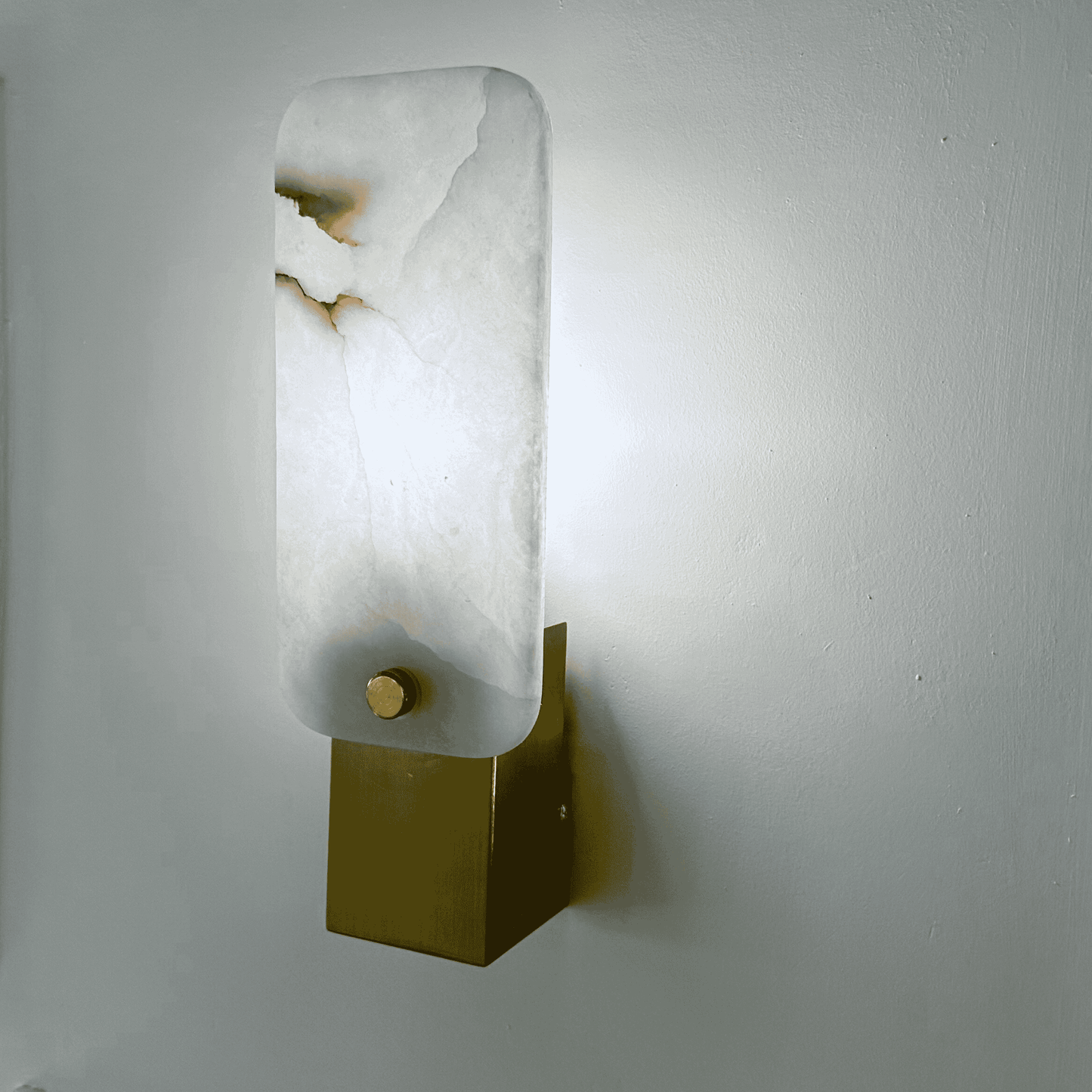 Side view of square marble sconce glowing softly with white stone and brass base.