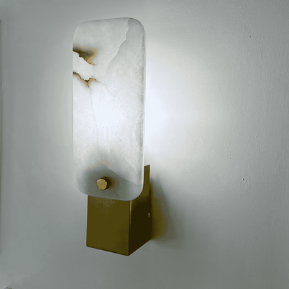 Side view of square marble sconce glowing softly with white stone and brass base.
