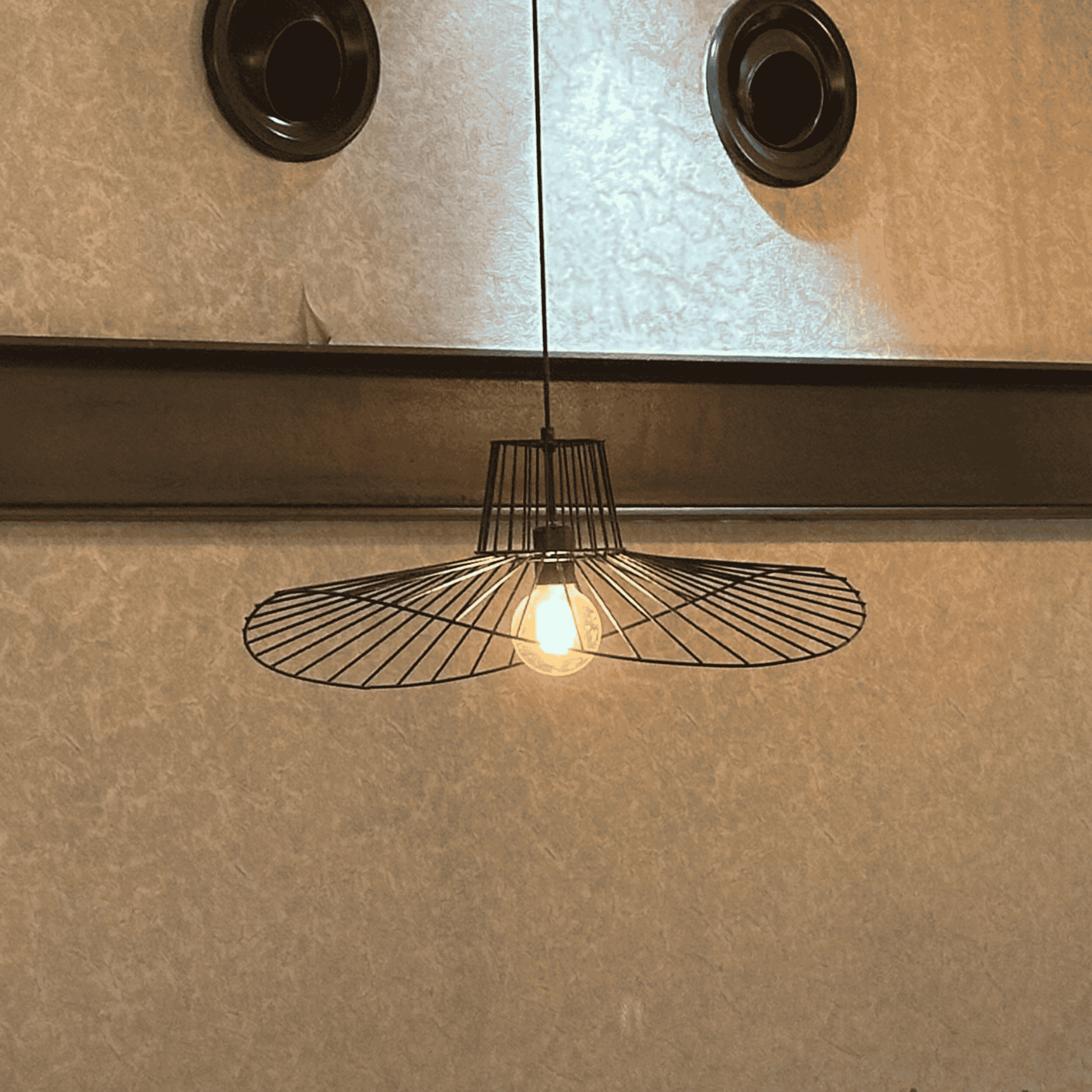Single wireframe straw hat pendant light casting warm glow on a textured wall background.