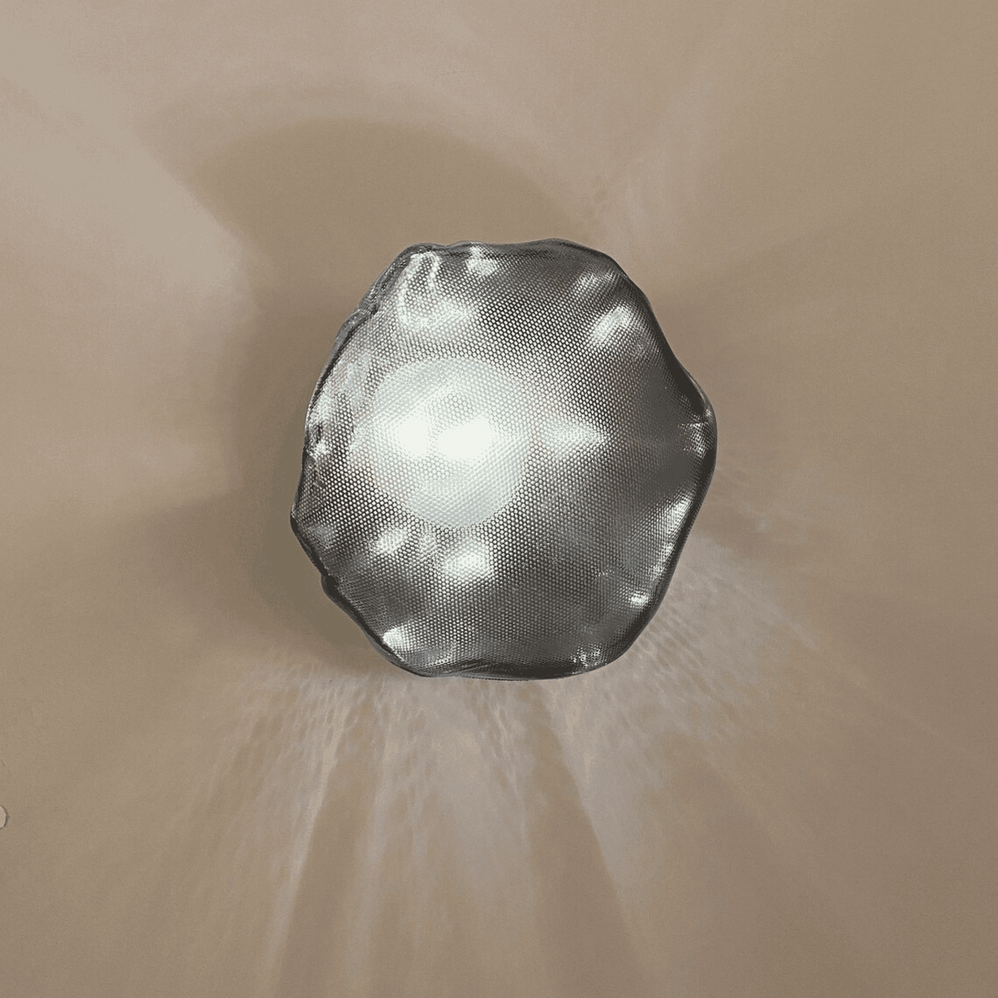 Smoky glass wall sconce in organic stone shape emits gentle light and shadow play.