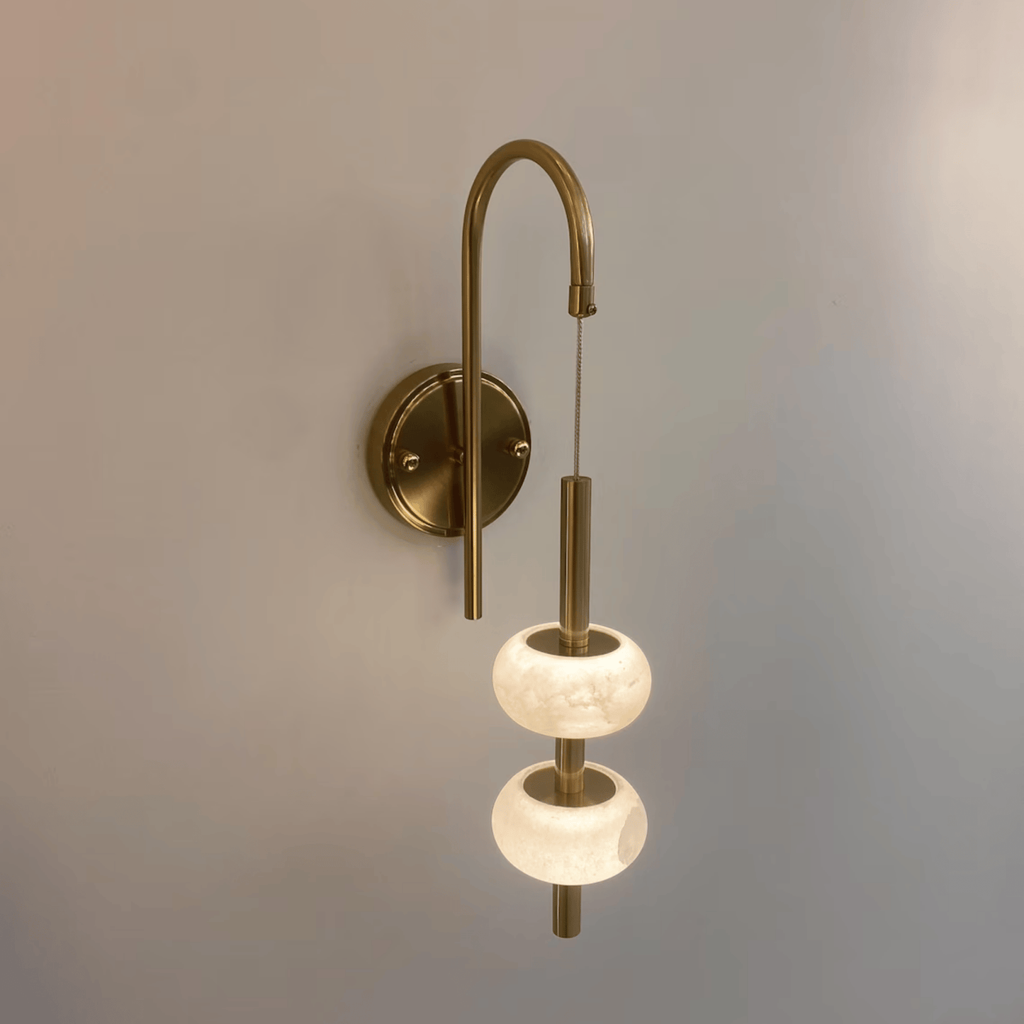 Modern alabaster wall sconce with warm light and suspended brass structure.