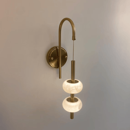 Modern alabaster wall sconce with warm light and suspended brass structure.