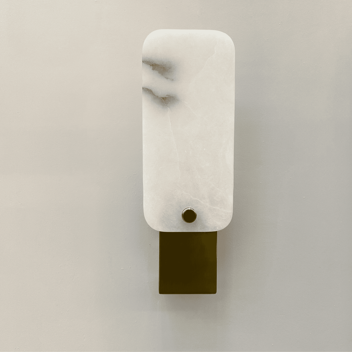 Square marble wall lamp with white stone shade and brushed brass base mounted on a neutral wall.