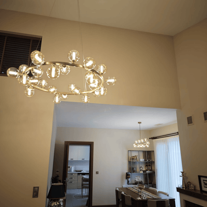 Modern chandelier with brass frame and clear glass globes hanging above a dining room in a high-ceiling space.