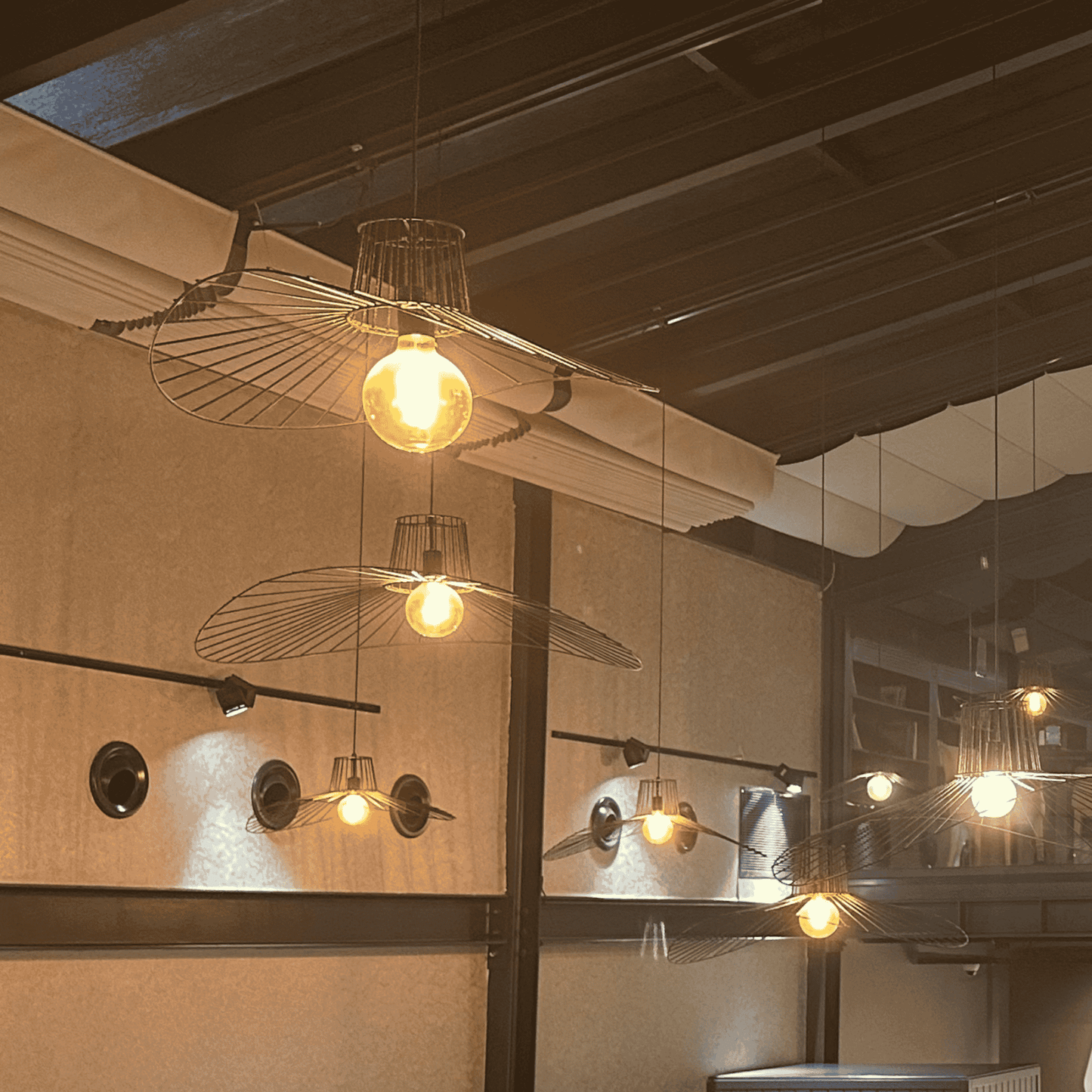 Double straw hat pendant lights with wireframe design and glowing filament bulbs in a stylish interior.