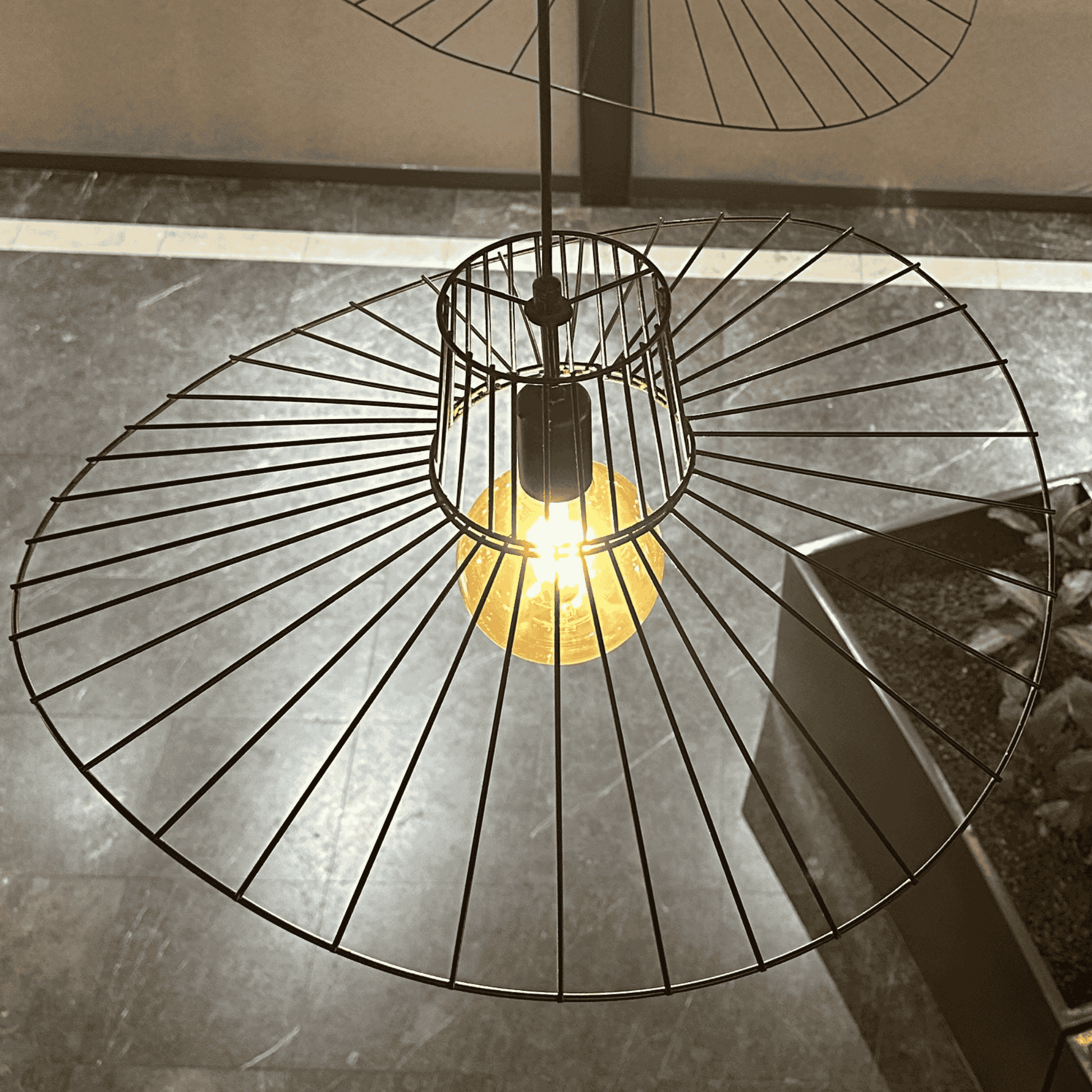 Wireframe straw hat pendant light with warm bulb, adding modern elegance to indoor spaces.