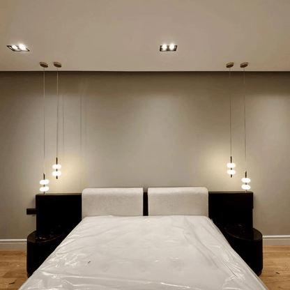 Symmetrical alabaster pendant lights hanging beside bed in minimalist bedroom interior.