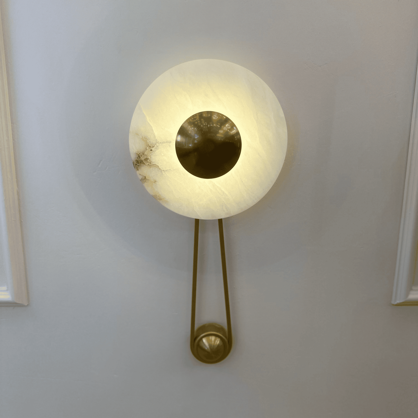 Front view of alabaster wall sconce with central round brass disc on a paneled interior wall.