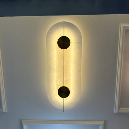 Vertical alabaster sconce with brass discs and soft backlighting for elegant wall illumination.