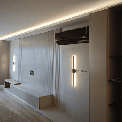 Vertical wall sconce with soft glow installed in a modern room with recessed ceiling lights and paneled walls under construction.