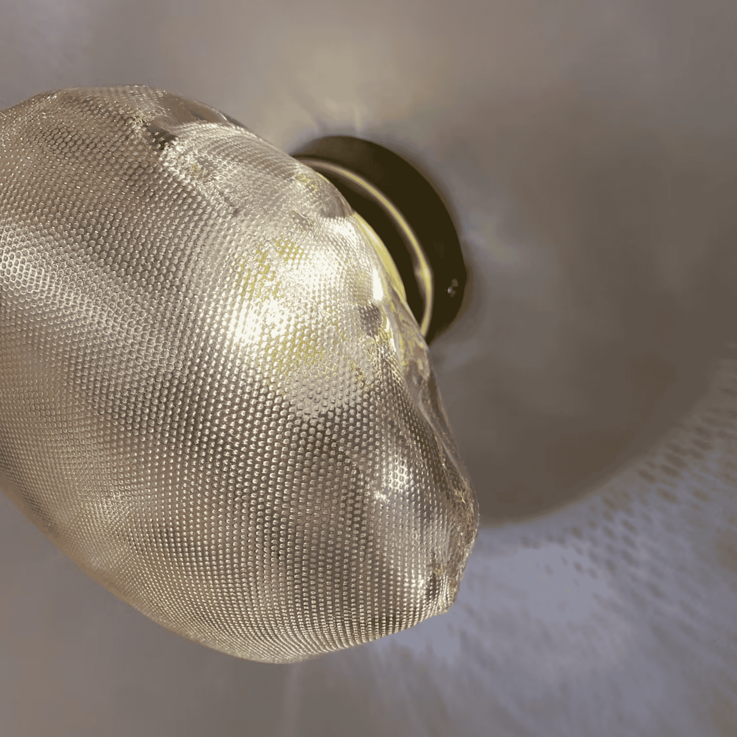 Detail view of a natural stone-shaped glass wall sconce with textural surface and warm illumination.