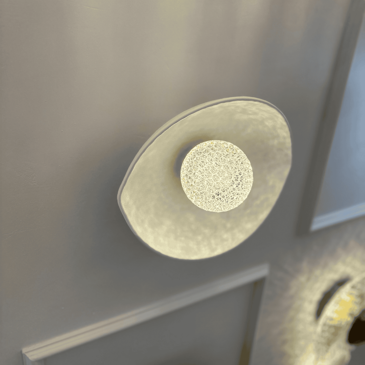 White plexiglass LED sconce showcasing intricate light diffusion from a central textured light source.